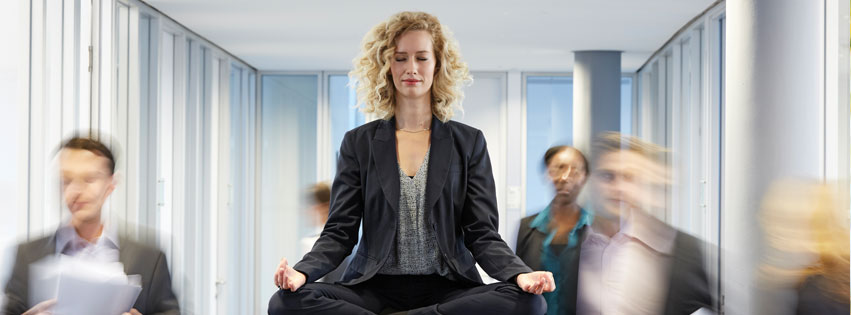Woman meditating on a conference table as coworkers rush by