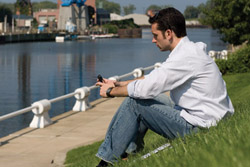 David Mills sits on the grass by a river