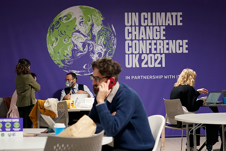 People working at small tables in front of a backdrop that says UN Climate Change Conference UK 2021