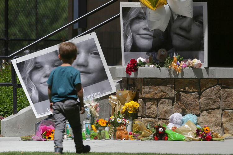 Child walking past a memorial with flowers, candles and pictures of two children