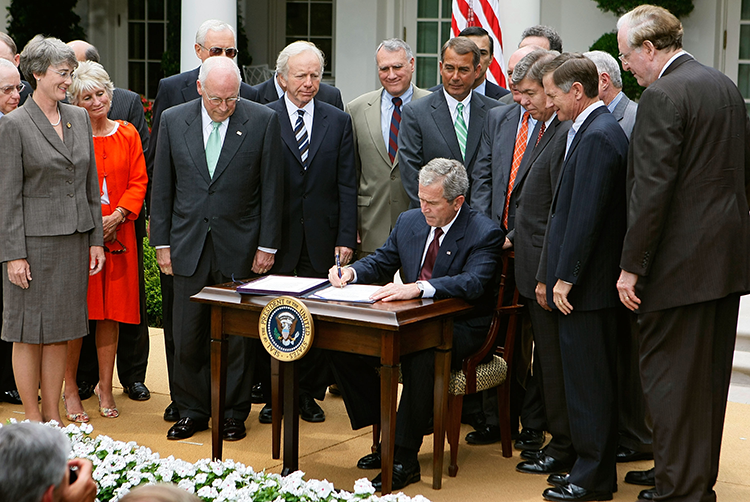 President George W. Bush surrounded by lawmakers and signing a document