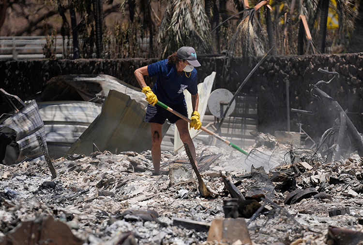 Masked woman shovels through ashes of building in Lahaina, Hawaii