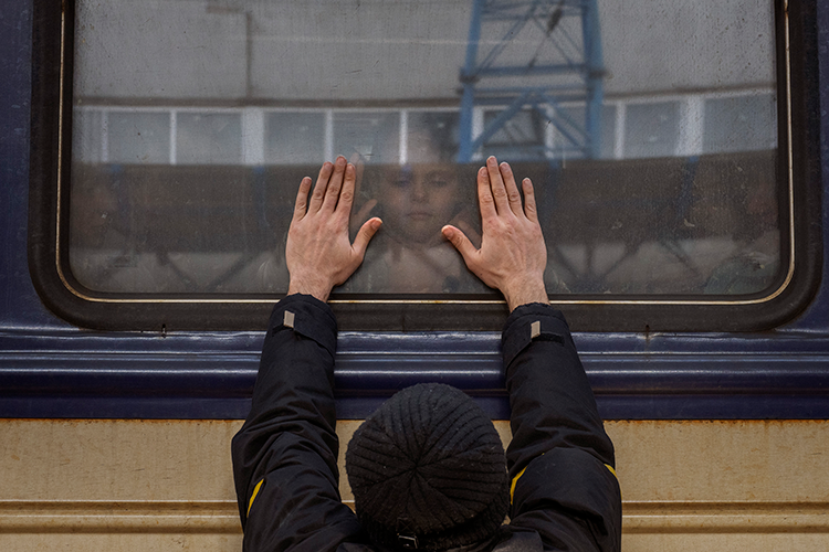 Father presses his hands to a train window as he says goodbye to his daughter