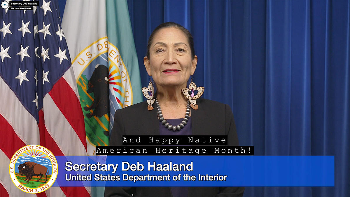 U.S. Secretary of the Department of the Interior Deb Haaland stands in front of flags.