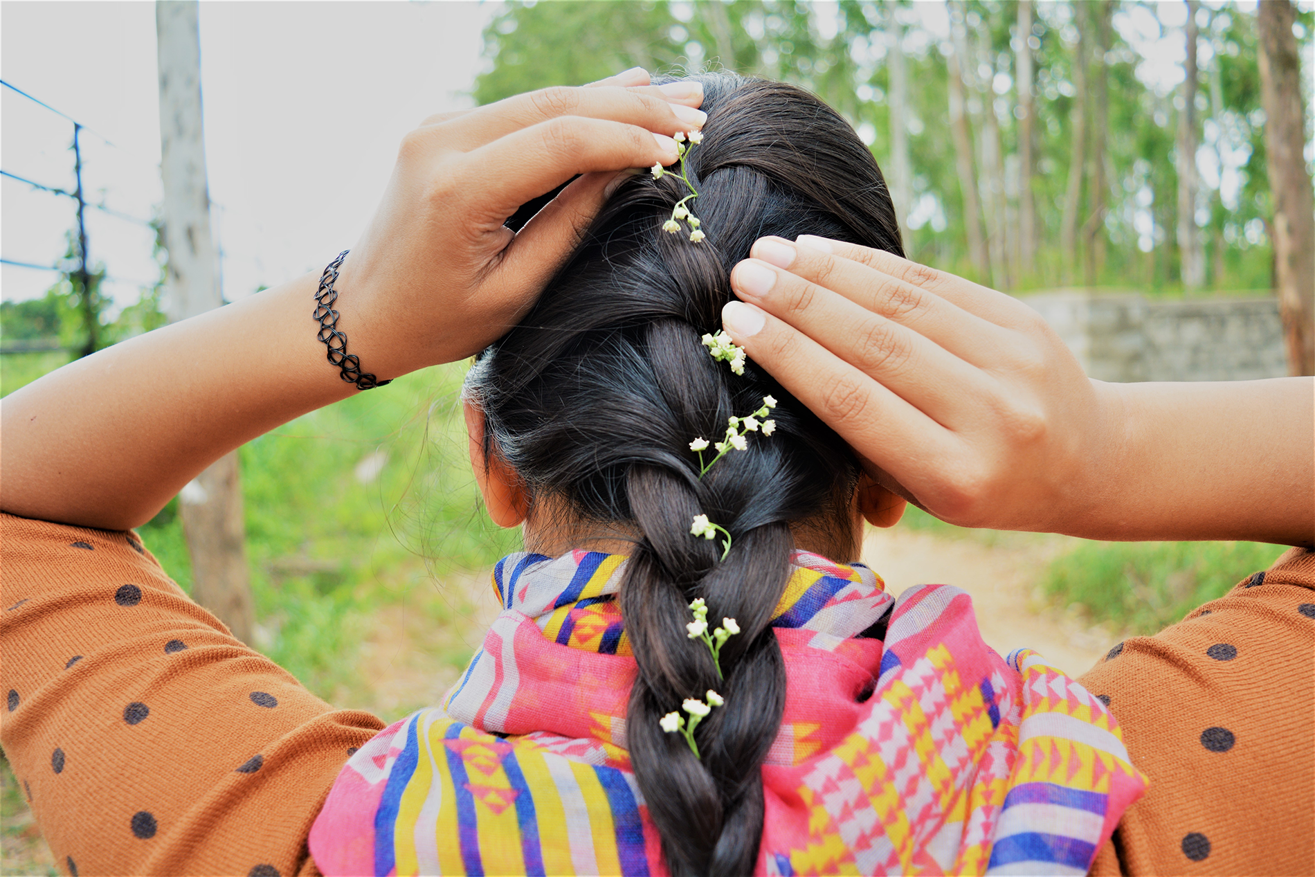 Woman seen from the back with tiny flowers woven into her long braid