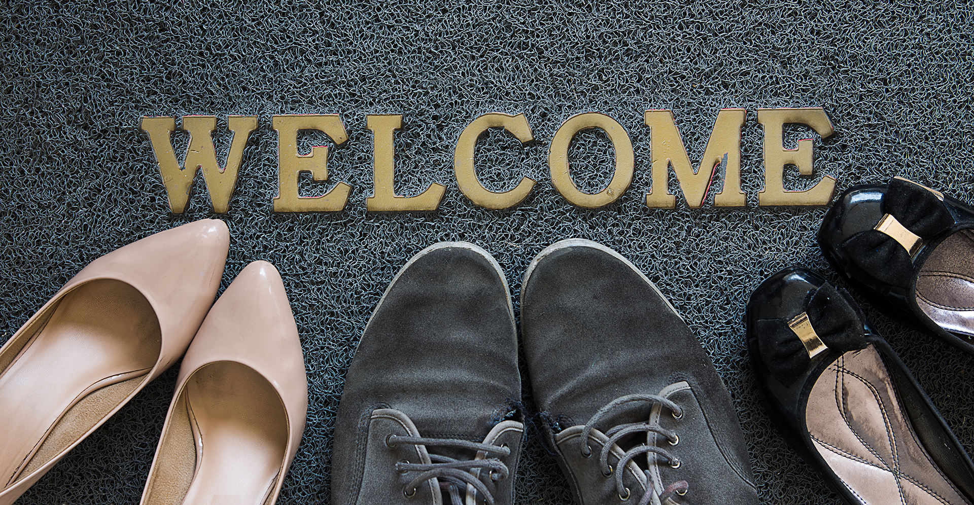A welcome mat with three pairs of shoes pointing to the WELCOME text