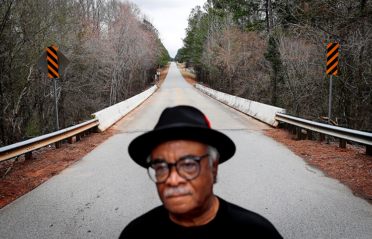 Black man in a hat stands pensively on a country road