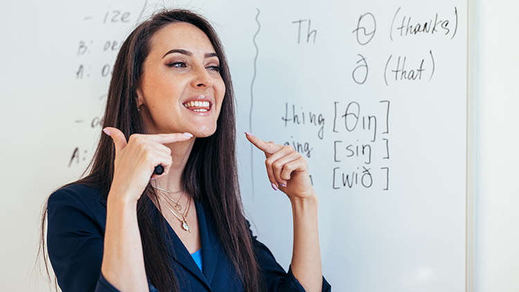 English teacher at whiteboard gestures to vocal cords.