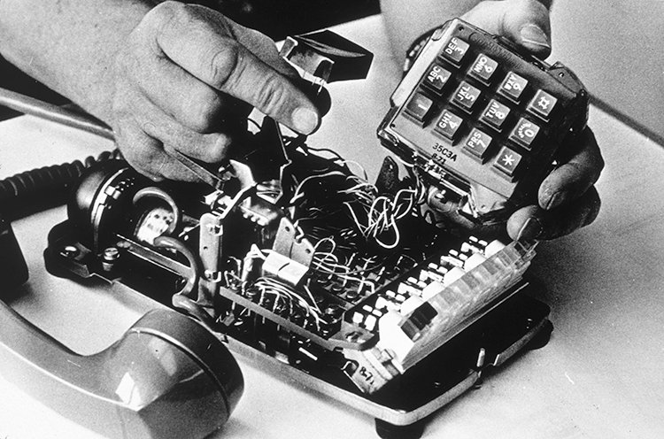 Man's hands placing a wiretap inside an old fashioned telephone